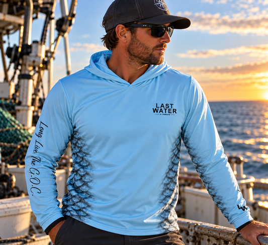 Front of the blue Last Water Tribute hooded fishing shirt, worn on a boat, with chest logo and fish-scale side panels.